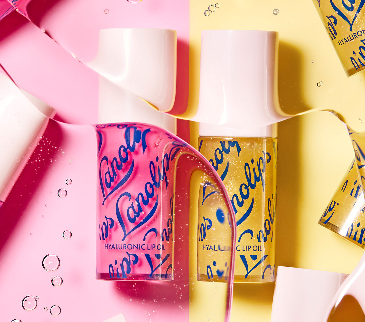 Lanolips Hyaluronic Lip Oil Duo in Raspberry and Honey, suspended in hyaluronic acid with pink and yellow background.