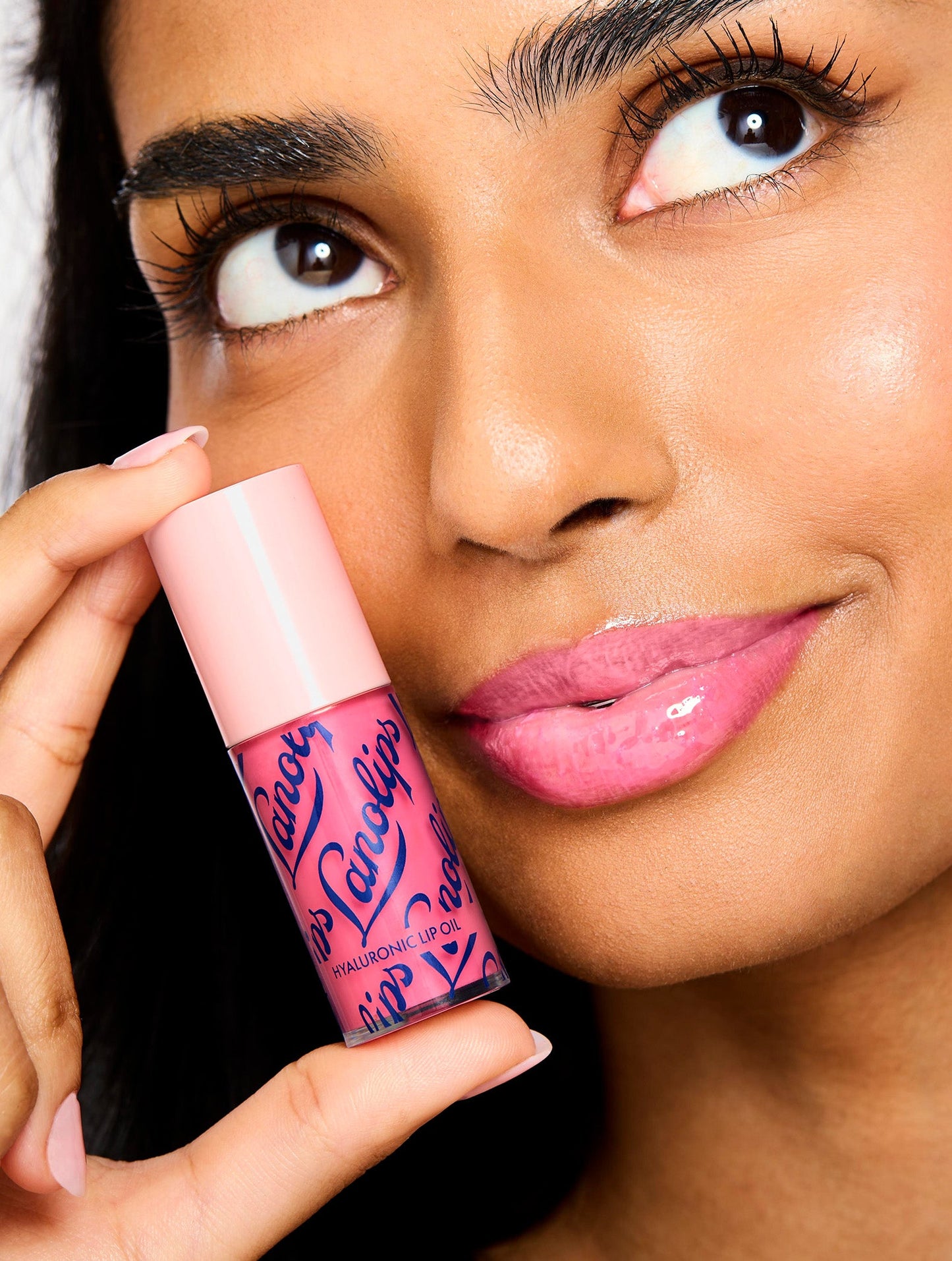 Model smiling while holding Lanolips Hyaluronic Lip Oil Raspberry, showing glossy, hydrated lips with a radiant finish