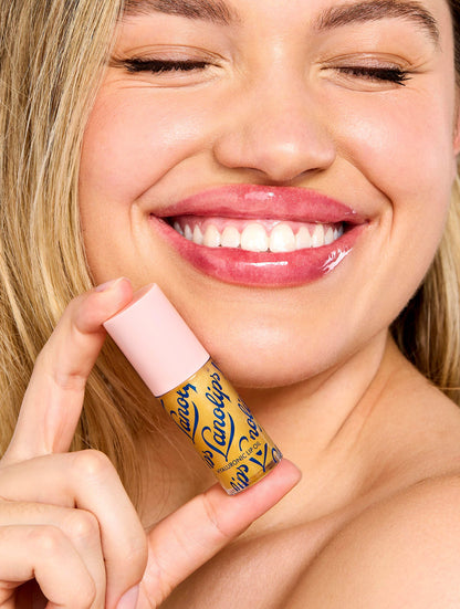 Model smiling while holding Lanolips Hyaluronic Lip Oil Honey, showing glossy, hydrated lips with a radiant finish