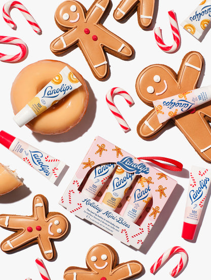 Flatlay of Lanolips Holiday Mini Bites lip balm trio gift set with Candy Cane, Gingerbread and Glazed Donut flavours, styled with gingerbread cookies and candy canes.
