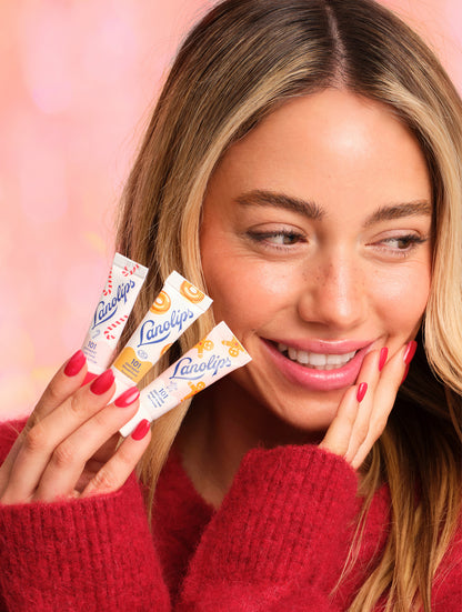 Model holding the 3g mini lip balms Lanolips 101 Delicious range in Candy Cane, Glazed Donut and Gingerbread. Keep your lips soft, nourished and with a sweet festive twist with this trio, designed for hydrating dry lips. 